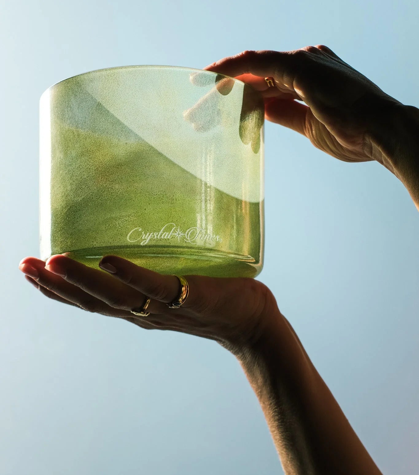 Hands holding a green alchemy crystal singing bowl in soft natural light – sound healing instrument