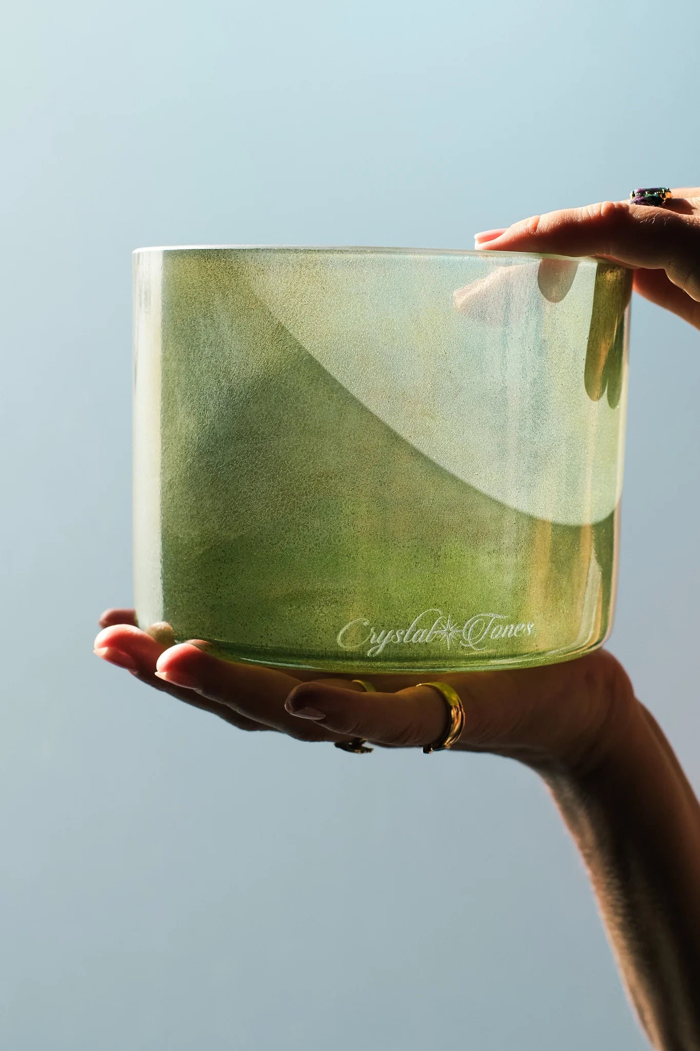 Hands holding a green alchemy crystal singing bowl in soft natural light – sound healing instrument
