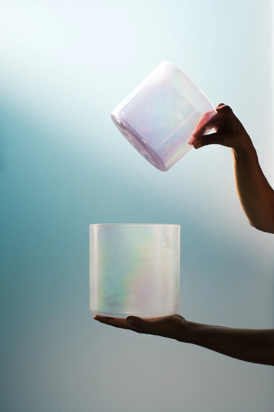 two hand holding shimmering alchemy crystal singing bowls against a bright background
