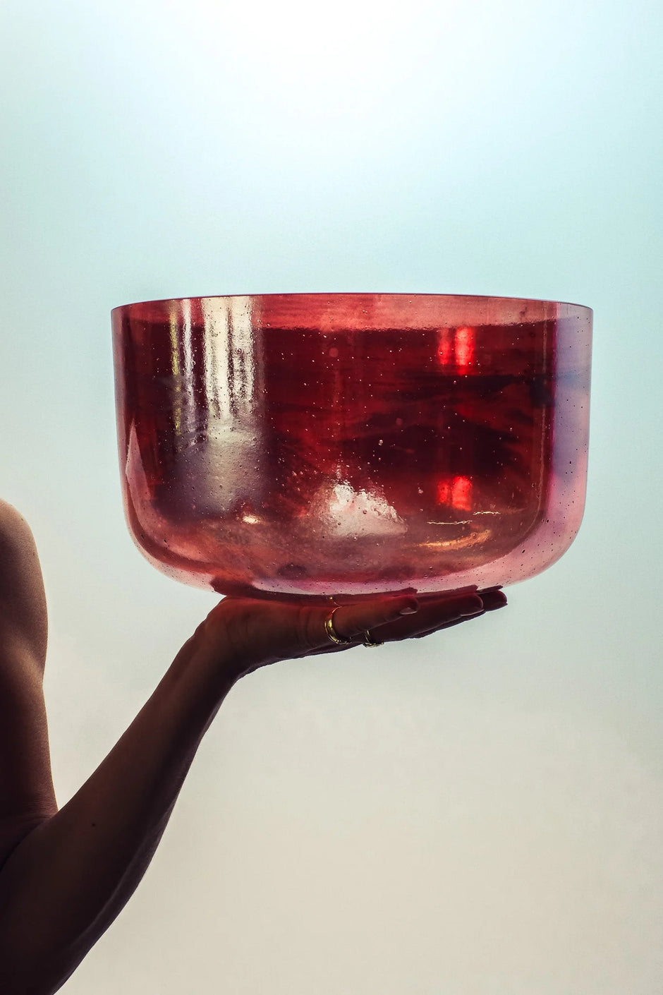 Hand holding a shimmering red crystal singing bowl against a bright background
